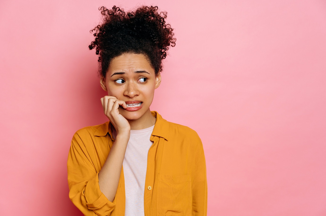 Stunned african american young woman, in casual wear, looking stressed and nervous with hands on mouth biting nails, looking aside, is going through, stands on isolated pink background