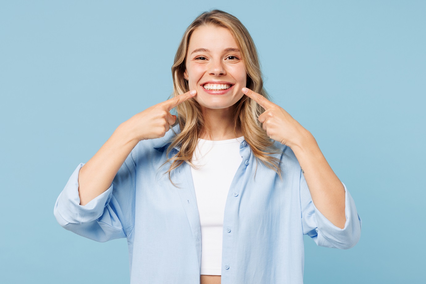 Young smiling satisfied happy woman she wearing white top shirt casual clothes point index fingers on opened mouth teeth isolated on plain pastel light blue cyan background studio. Lifestyle concept