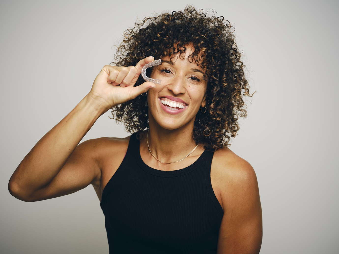 Smiling Woman Holding an Invisible Teeth Aligner